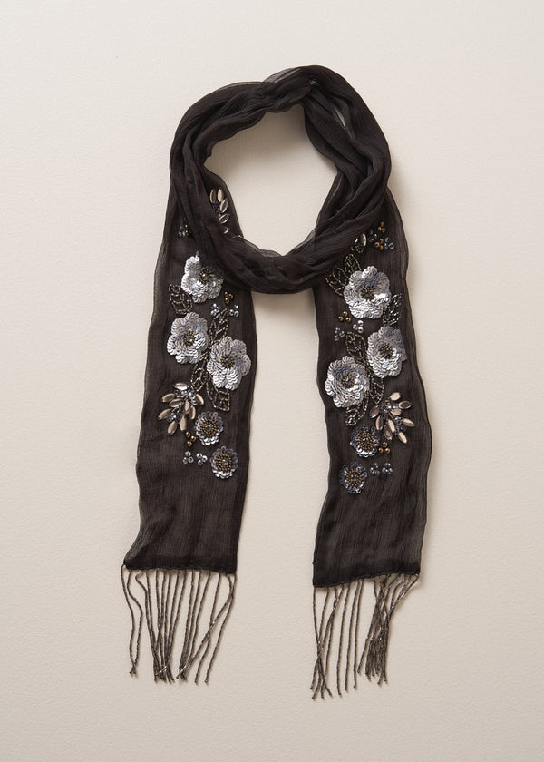 Black scarf adorned with sequin flower detail and beaded tassels on a beige background