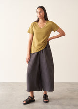 A woman wearing a olive green v-neck t-shirt with grey charcoal stripe trousers and sandals