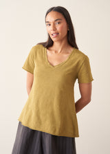 A woman wearing a olive green v-neck t-shirt with grey charcoal stripe trousers and sandals