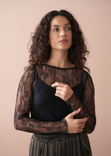 Woman wearing a black lace top with satin trousers, against a beige background