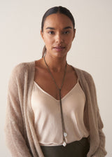 Model wearing a beaded pearl drop necklace with satin top and soft knit cardigan, on a beige background
