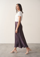 Woman wearing burgundy satin slip skirt with white t-shirt and stone knittted waistcoat