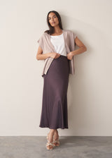 Woman wearing burgundy satin slip skirt with white t-shirt and stone knittted waistcoat