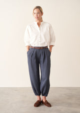 A woman wearing dark blue balloon leg trousers with pleat details and a white cotton shirt.