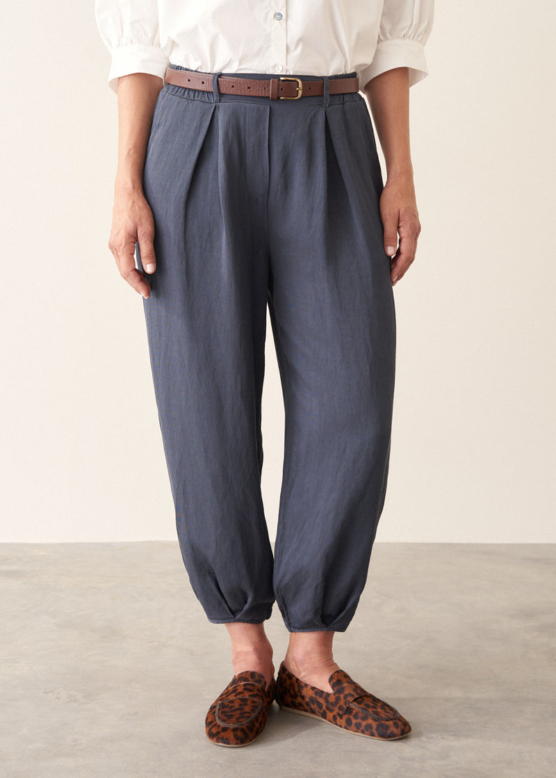 A woman wearing dark blue balloon leg trousers with pleat details and a white cotton shirt.