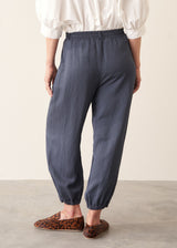 A woman wearing dark blue balloon leg trousers with pleat details and a white cotton shirt.