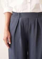 A woman wearing dark blue balloon leg trousers with pleat details and a white cotton shirt.
