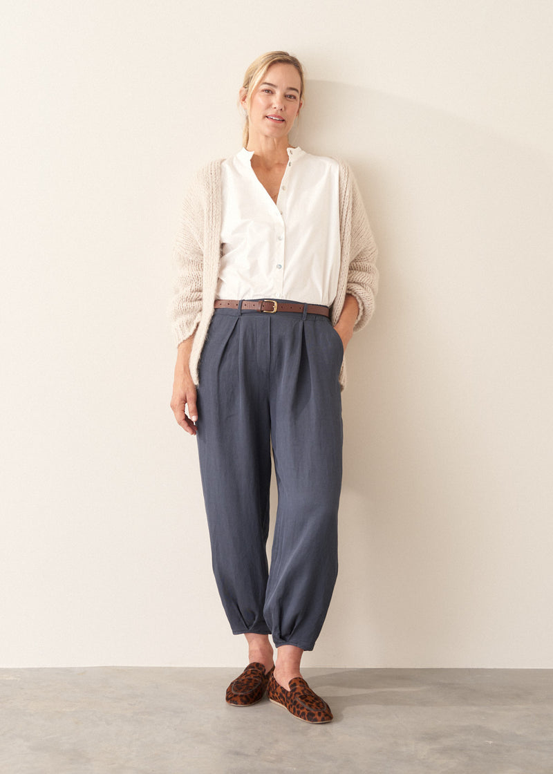 A woman wearing dark blue balloon leg trousers with pleat details and a white cotton shirt.