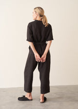 Woman wearing a short sleeve black linen jumpsuit with a button up front and waist tie