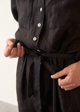 Woman wearing a short sleeve black linen jumpsuit with a button up front and waist tie