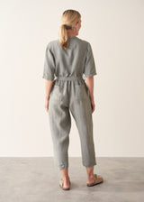 Woman wearing a light sage green linen jumpsuit with a waist tie and pockets