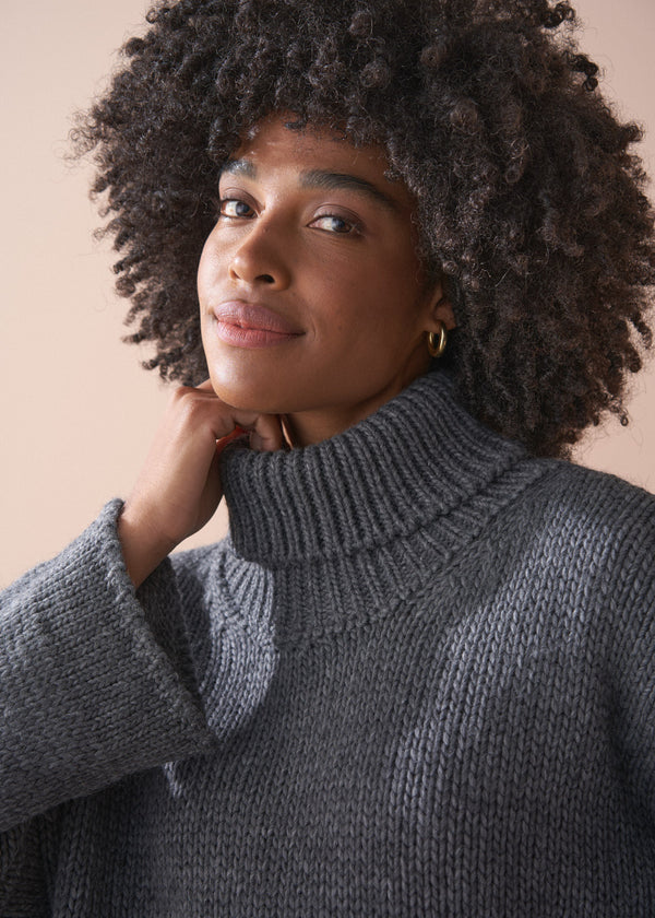 Person wearing a grey chunky knit sweater and satin bias cut skirt against a beige background