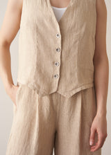 Woman wearing a beige striped linen waistcoat with a white vest top and striped linen trousers