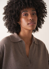 Woman wearing brown sweater and gold minimal necklace with a simple oval pendant on a beige background