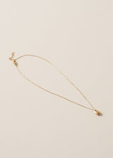 Delicate gold chain with gold oval pendant, placed on a beige background