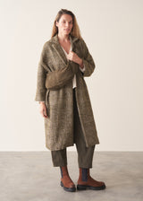 A woman wearing an oversized checked coat with dark green trousers, ginger boots and a white top against a plain background.