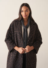 A women wearing a long dark brown leopard print coat with black trousers and a white blouse.
