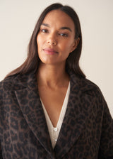 A women wearing a long dark brown leopard print coat with black trousers and a white blouse.