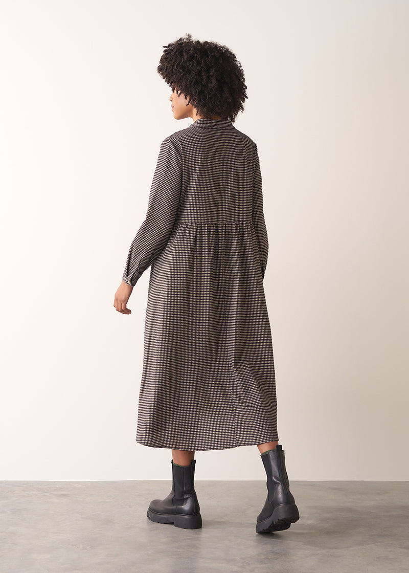 Woman wearing a checked midi dress and chunky boots against a plain background