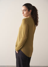 Woman wearing an olive green long-sleeve top with jeans against a plain background