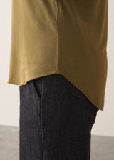 Woman wearing an olive green long-sleeve top with jeans against a plain background