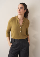 Woman wearing an olive green long-sleeve top with jeans against a plain background