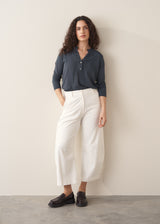 Woman wearing dark grey long sleeve top and white barrel leg jeans