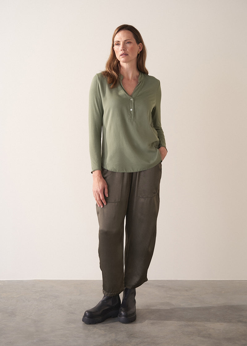 Woman wearing a moss green long-sleeve jersey top against a plain background
