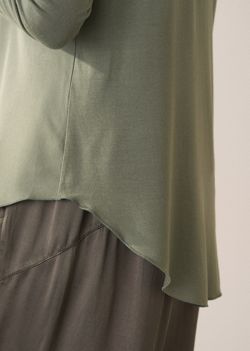 Woman wearing a moss green long-sleeve jersey top against a plain background