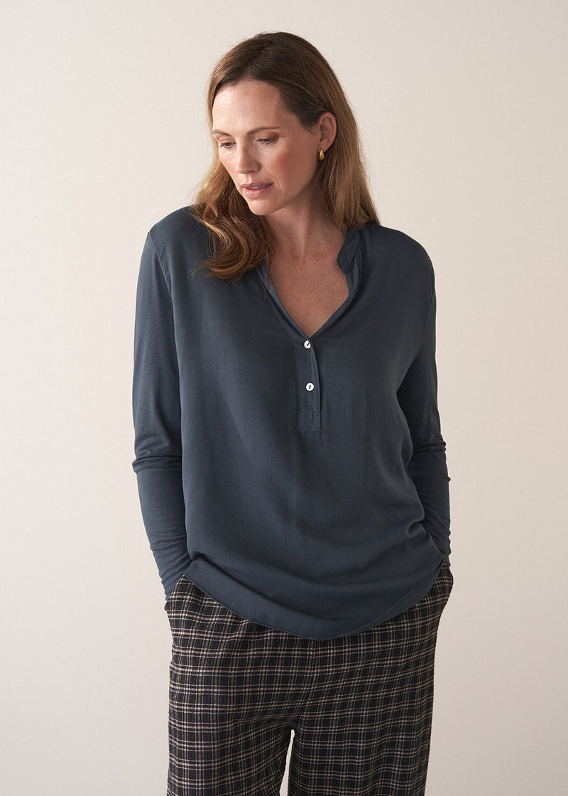 Woman wearing dark grey blue long sleeve jersey top against a plain background