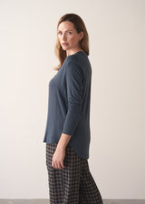 Woman wearing dark grey blue long sleeve jersey top against a plain background