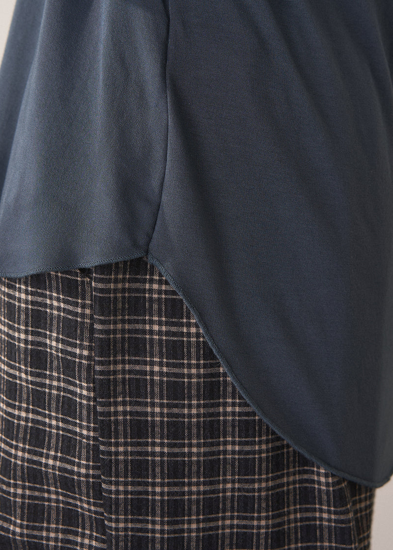 Woman wearing dark grey blue long sleeve jersey top against a plain background