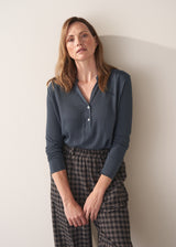 Woman wearing dark grey blue long sleeve jersey top against a plain background