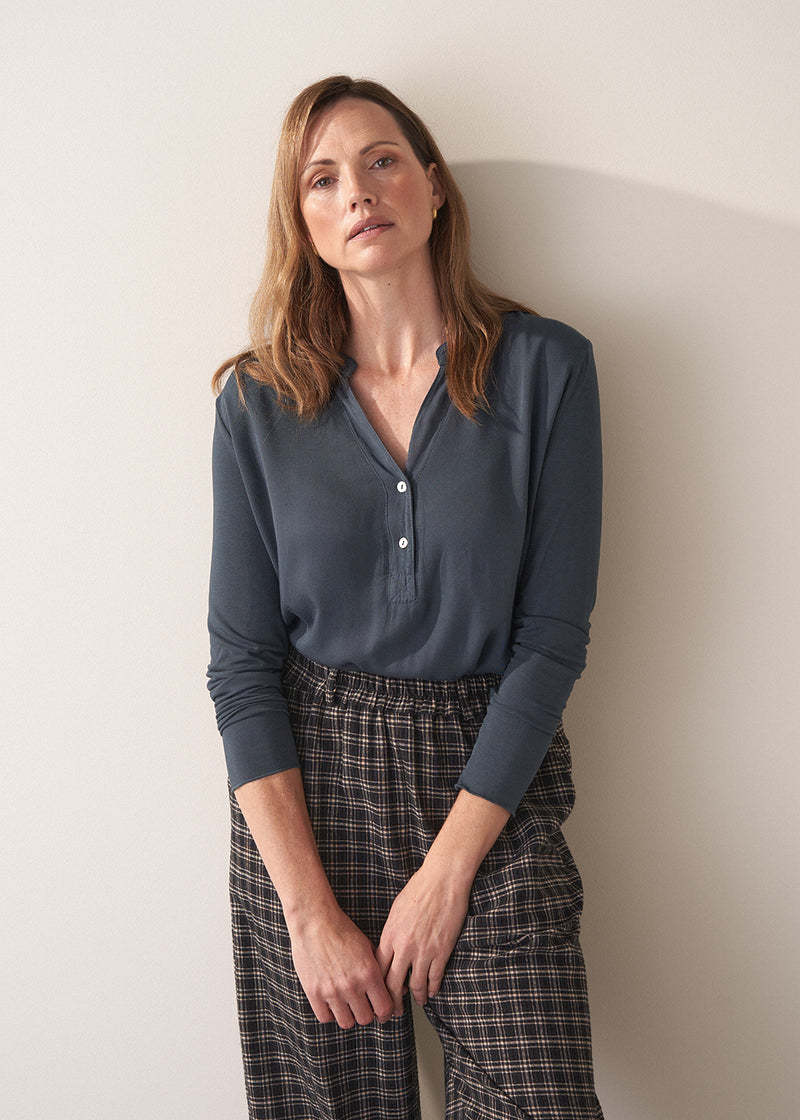 Woman wearing dark grey blue long sleeve jersey top against a plain background