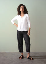 Woman wearing long sleeve white top with button detail, paired with dark denim trousers and sandals