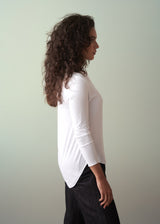 Woman wearing a long sleeve white top with button detail, paired with dark jeans