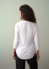 Woman wearing a long sleeve white top with button detail styled with dark trousers