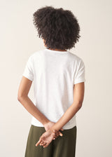 Woman wearing white, round neck t-shirt and dark green wide leg trousers against a plain background