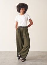 Woman wearing white, round neck t-shirt and dark green wide leg trousers against a plain background
