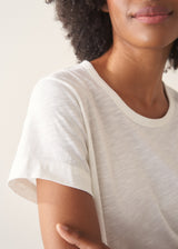 Woman wearing white, round neck t-shirt and dark green wide leg trousers against a plain background