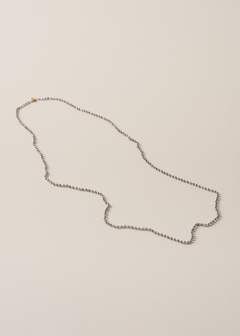 An ultra-long, fine gold chain necklace adorned with twinkling silver beads, on a beige background