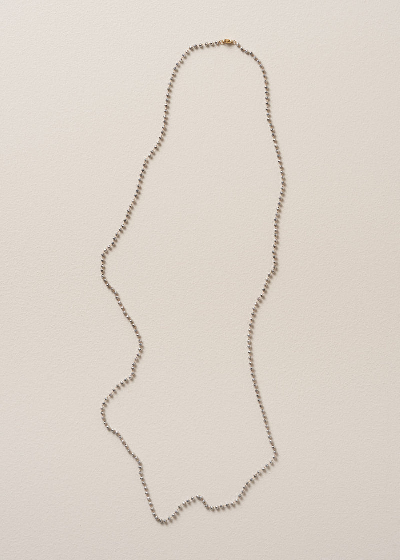 An ultra-long, fine gold chain necklace adorned with twinkling silver beads, on a beige background