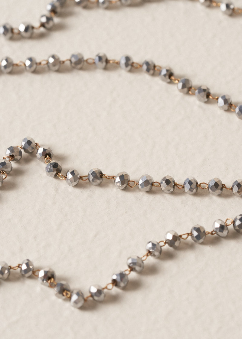Close up of an ultra-long, fine gold chain necklace adorned with twinkling silver beads on beige background