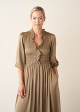 A woman wearing a light khaki green olive satin midi dress with smocked detail and ruffle collar