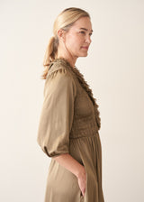 A woman wearing a light khaki green olive satin midi dress with smocked detail and ruffle collar