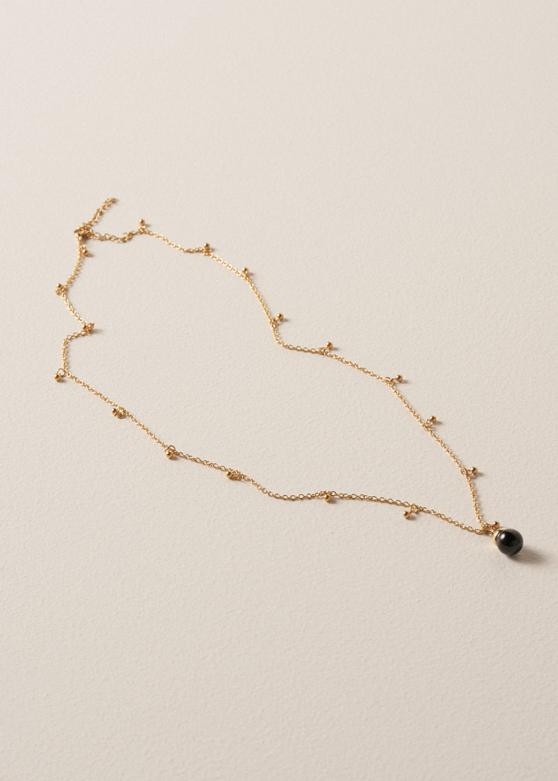 Long golden chain necklace with gold beads and a black pendant on a beige background