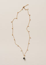 Long golden chain necklace with gold beads and a black pendant on beige background