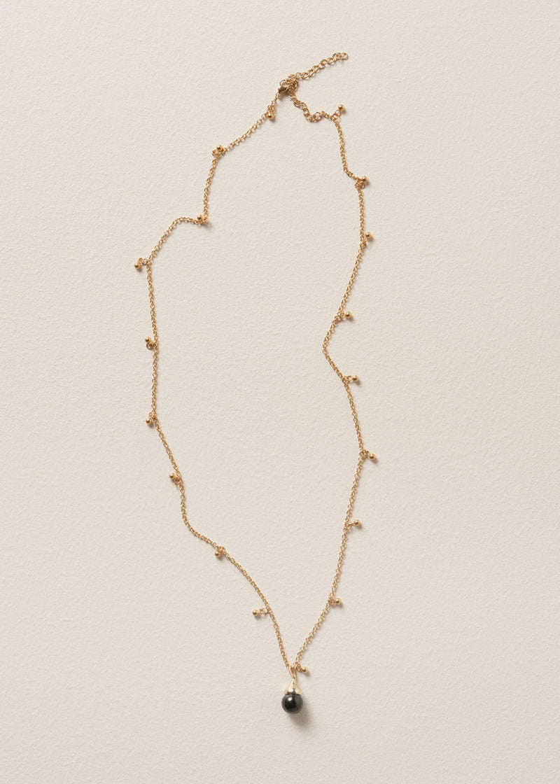 Long golden chain necklace with gold beads and a black pendant on beige background