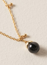 Close up of long golden chain necklace with gold beads and a black pendant