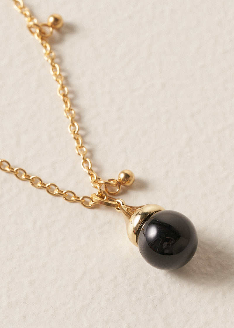 Close up of long golden chain necklace with gold beads and a black pendant